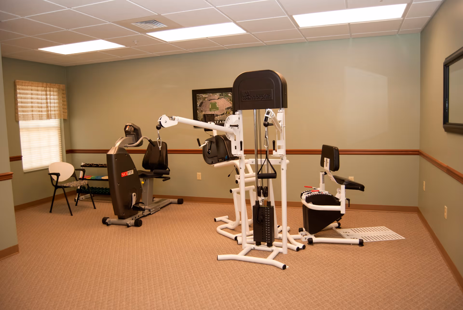 A carpeted interior exercise room with multiple workout machines and a couple of chairs.