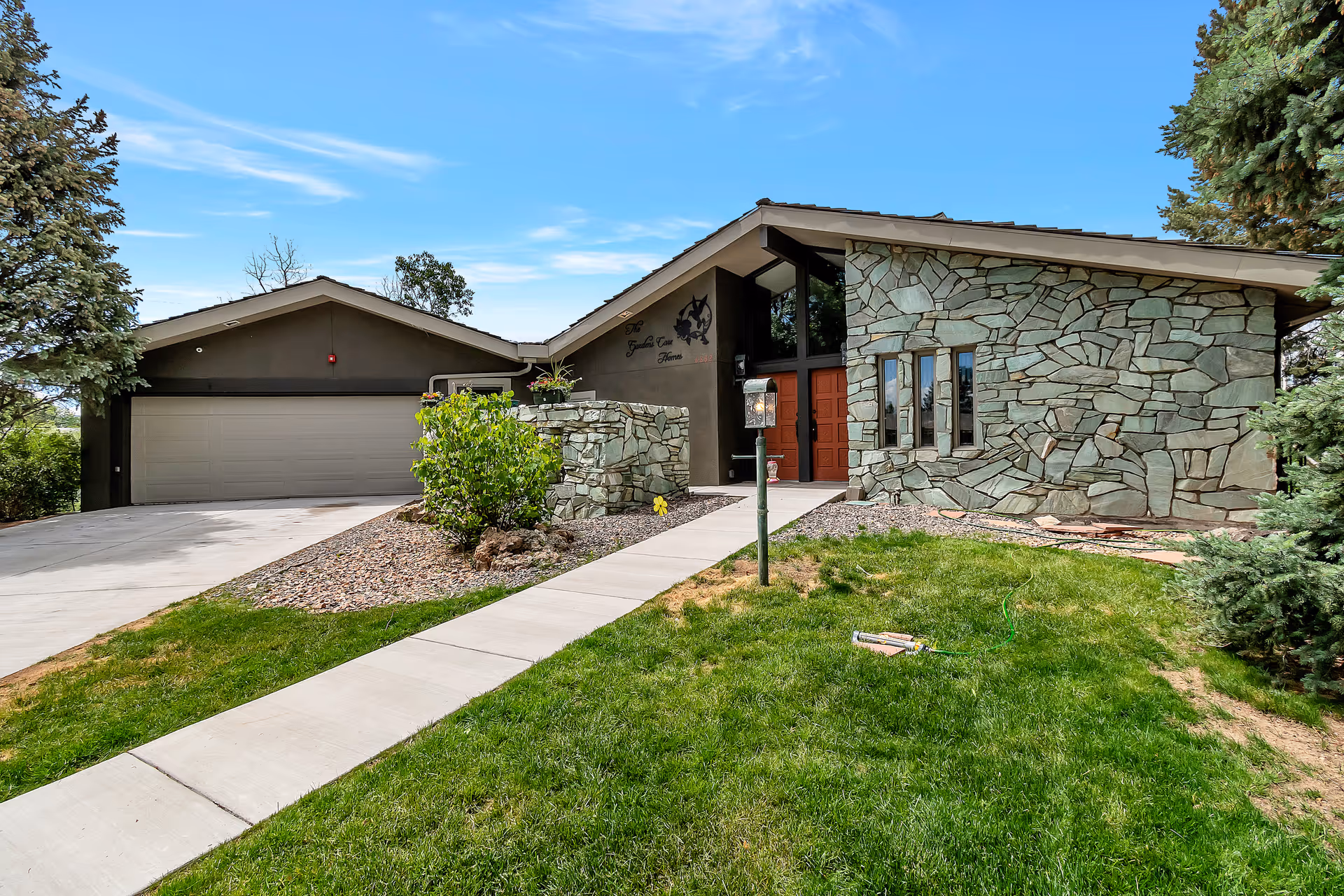 Front exterior of a single-story home with a stone facade, red double entry doors, attached garage, and a concrete walkway across a green lawn.
