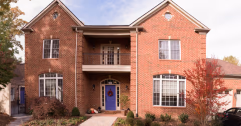 Two-story brick assisted-living building with balcony and blue front door.