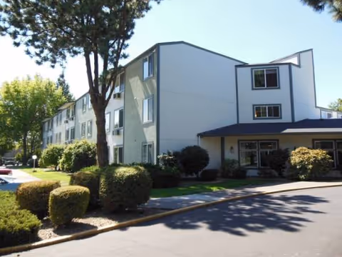 Exterior view of a light blue multi-story retirement facility with landscaped front.