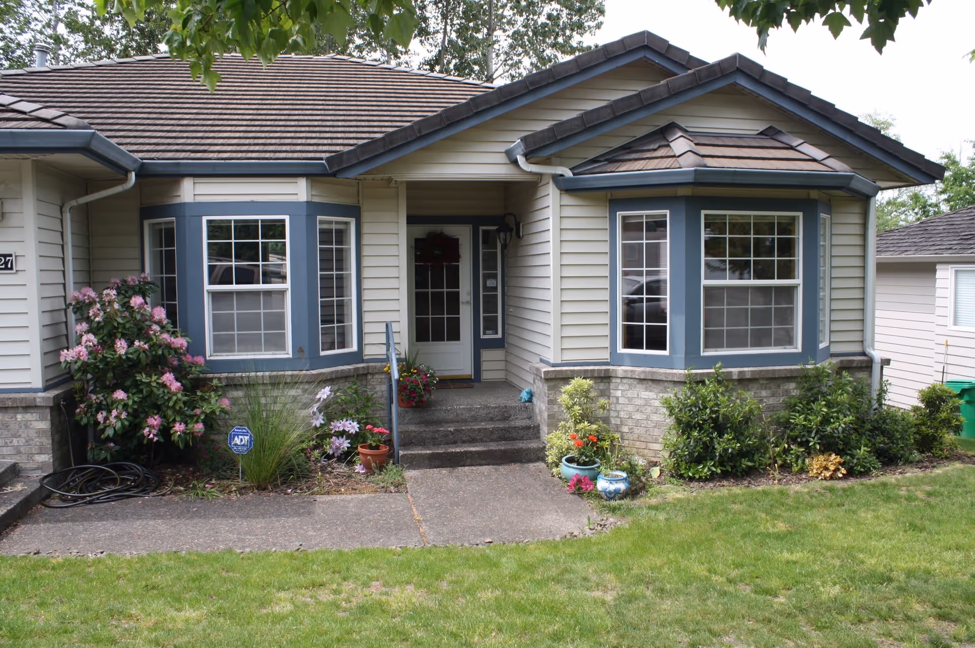 Front exterior of a single-story house with a central entrance, two bay windows, and a landscaped front yard.