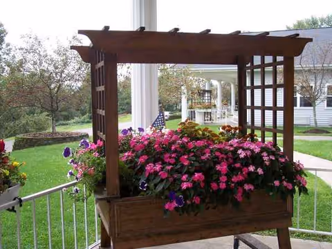 Wooden planter filled with colorful flowers on a porch overlooking a grassy yard.