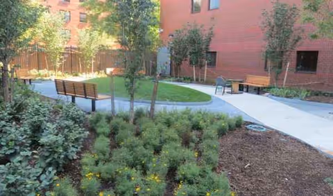 Brick building surrounds a landscaped outdoor courtyard with benches and trees.
