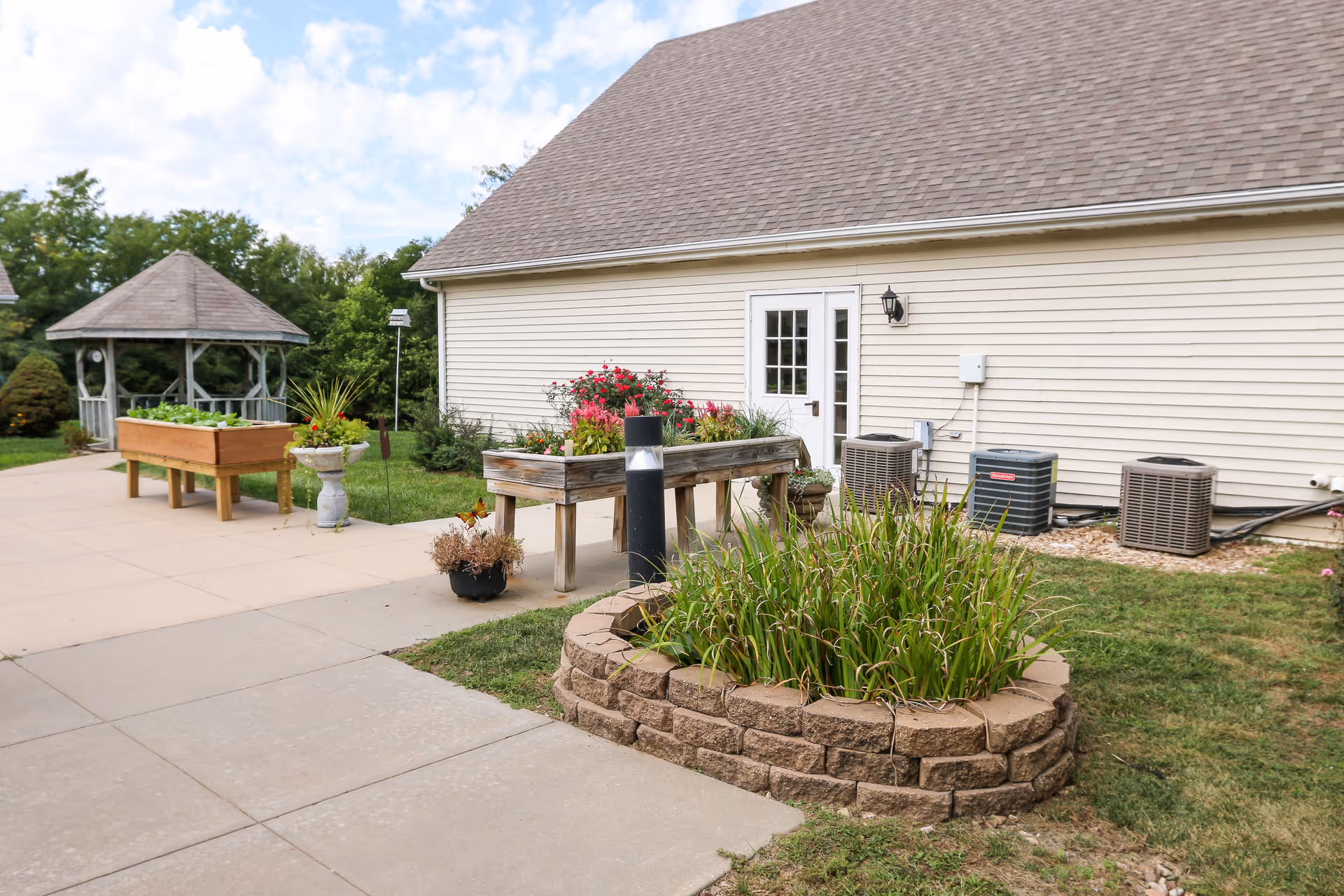 Outdoor garden area beside a light-colored building with raised planters, a gazebo, and a paved walkway.