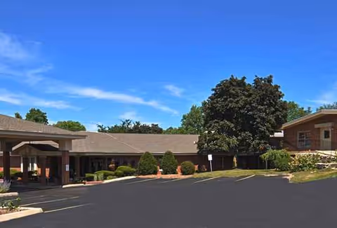 Exterior of a single-story senior living facility with a parking lot and trees.