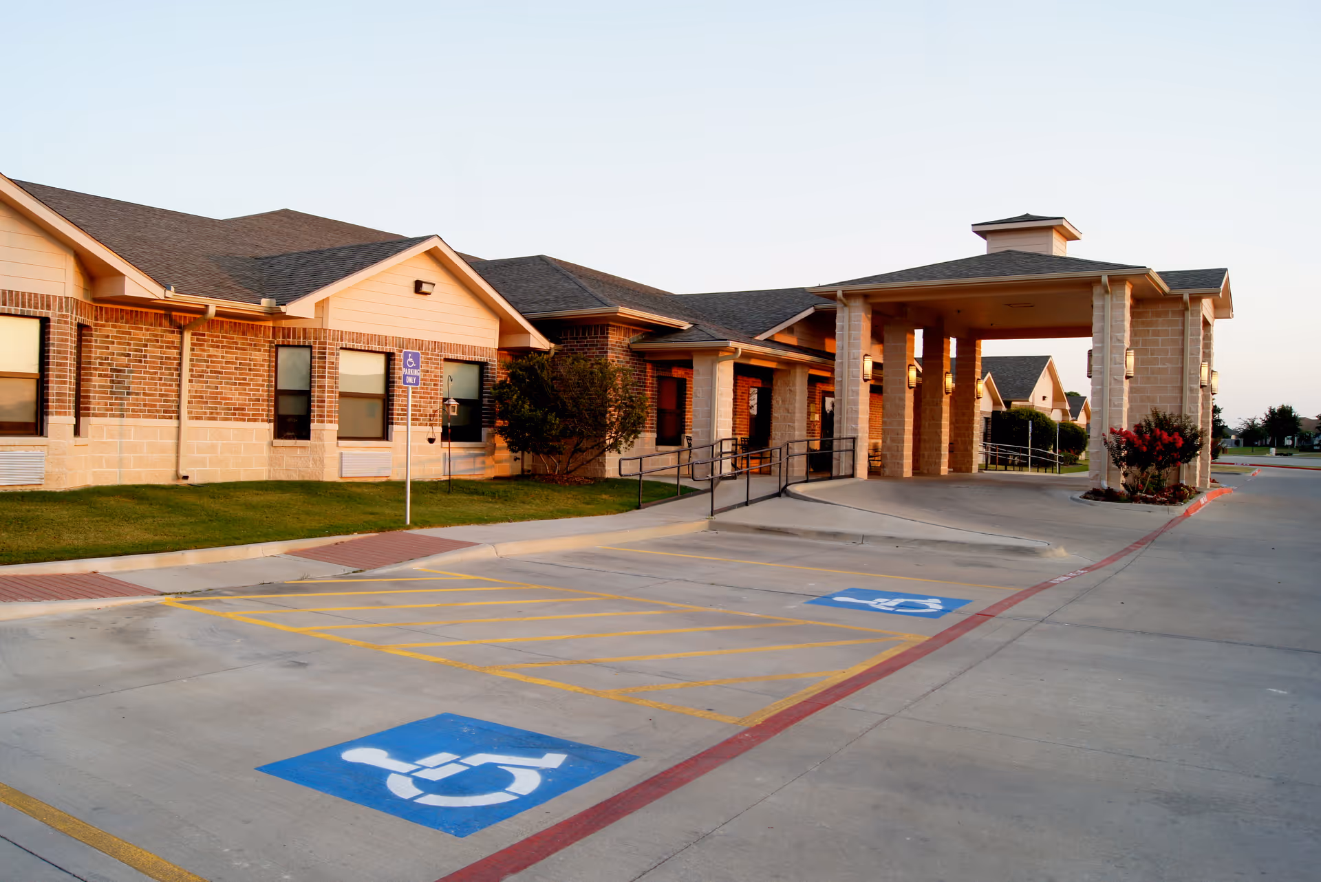 Front exterior of a brick rehabilitation and wellness center showing a covered entrance with a drive-through, wheelchair ramp, and accessible parking spaces.