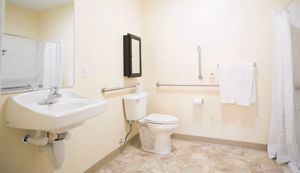 Accessible bathroom with a wall-mounted sink, toilet, grab bars, towel, and shower curtain.