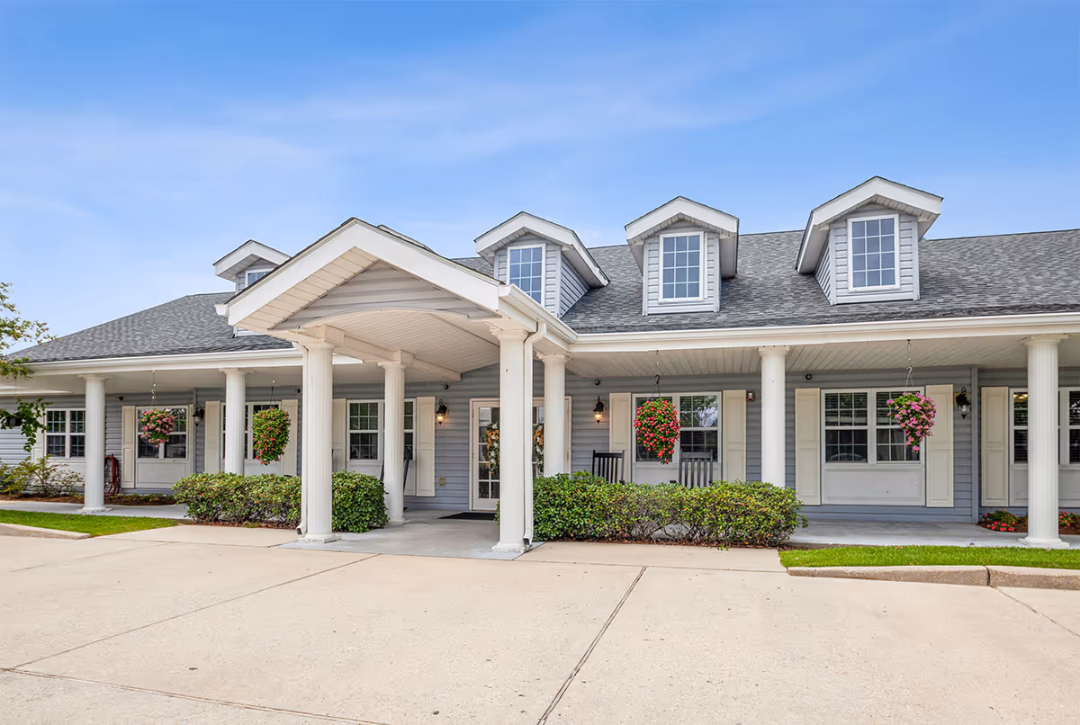 Front view of a senior living facility entrance with columns and hanging planters.