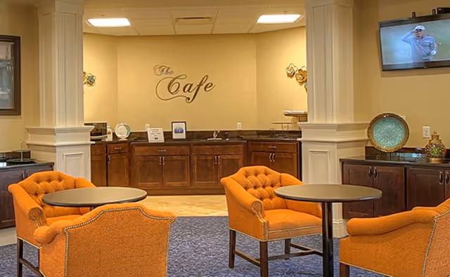 Interior cafe-style dining area with orange upholstered chairs, round tables, and a service counter labeled "The Cafe".