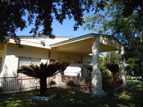 A single-story nursing home exterior with a covered entrance and surrounding trees.