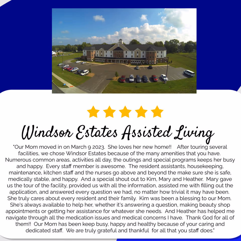 Aerial view of Windsor Estates Assisted Living building with a parking lot in front, surrounded by green lawns and trees under a partly cloudy sky.
