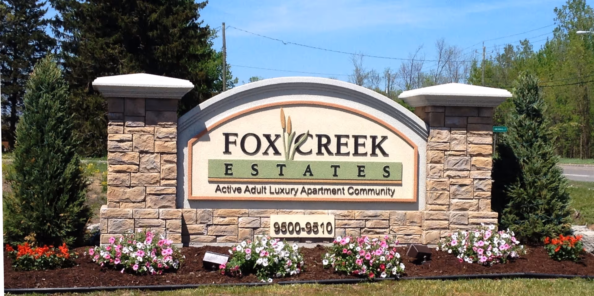 Stone entrance sign reading "Fox Creek Estates" surrounded by landscaped flowers and shrubs.
