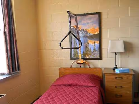 Nursing home patient room with red bed, trapeze, and nightstand.
