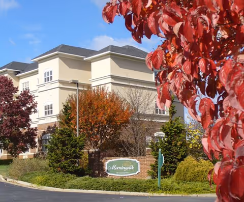 Exterior front of a multi-story beige senior living building with a 'Morningside' sign and autumn foliage.