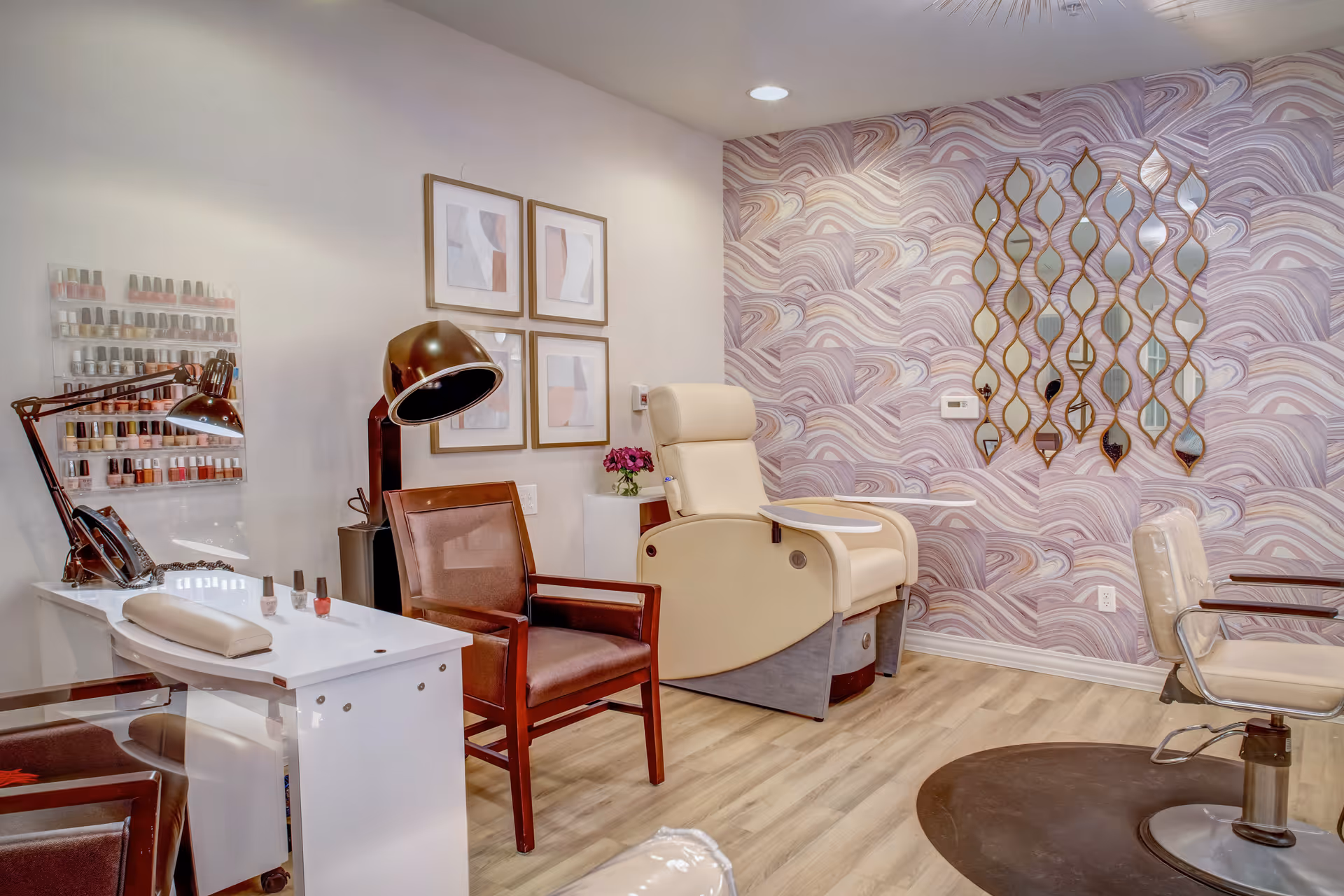 Bright salon interior with a manicure table, nail polish display, seating and a pedicure chair against a patterned accent wall.