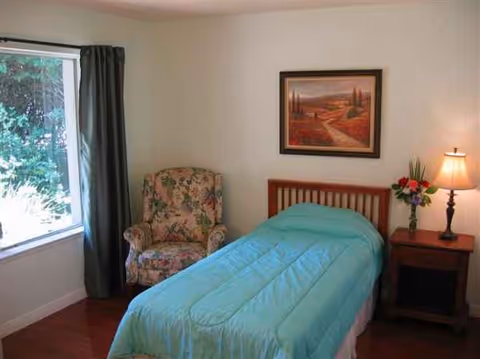 A small bedroom in a senior home with a single bed, chair, and nightstand.
