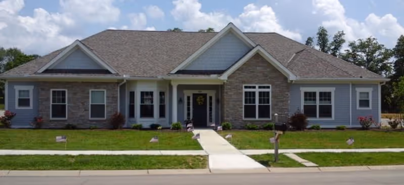 Front exterior of a single-story senior living facility with lawn and walkway.