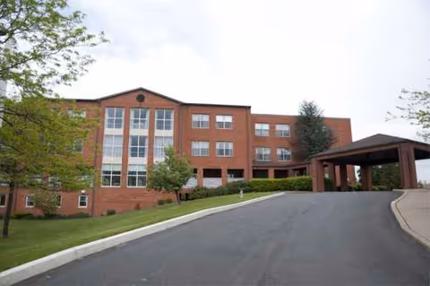 Red brick senior living building with a long driveway and covered entrance.