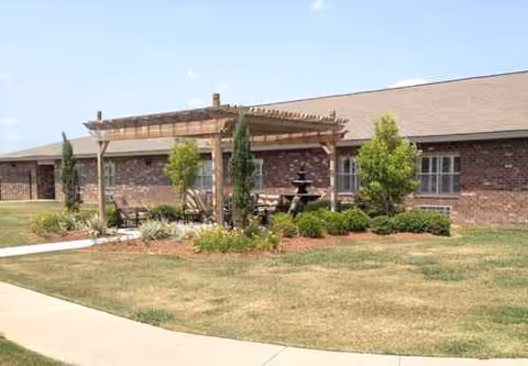 Brick senior living facility exterior with lawn and wooden pergola.