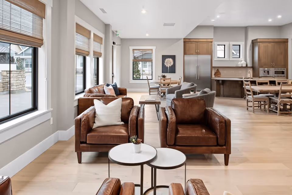 Open bright common room with leather armchairs, small tables, a dining area, and an open kitchen.
