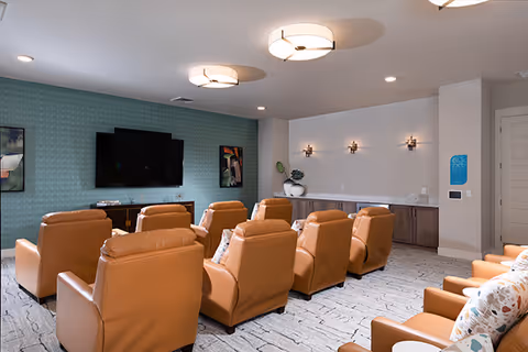 A media room with rows of tan leather recliners facing a wall-mounted TV and a patterned accent wall.