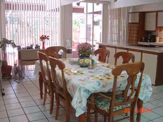 A sunny dining room with a floral tablecloth and wooden chairs.