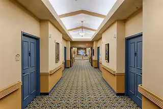 Long carpeted hallway with blue doors and warm lighting inside a senior facility.