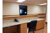 Empty reception or nurse station area with a granite countertop desk, office chair, telephone, and a hallway opening.