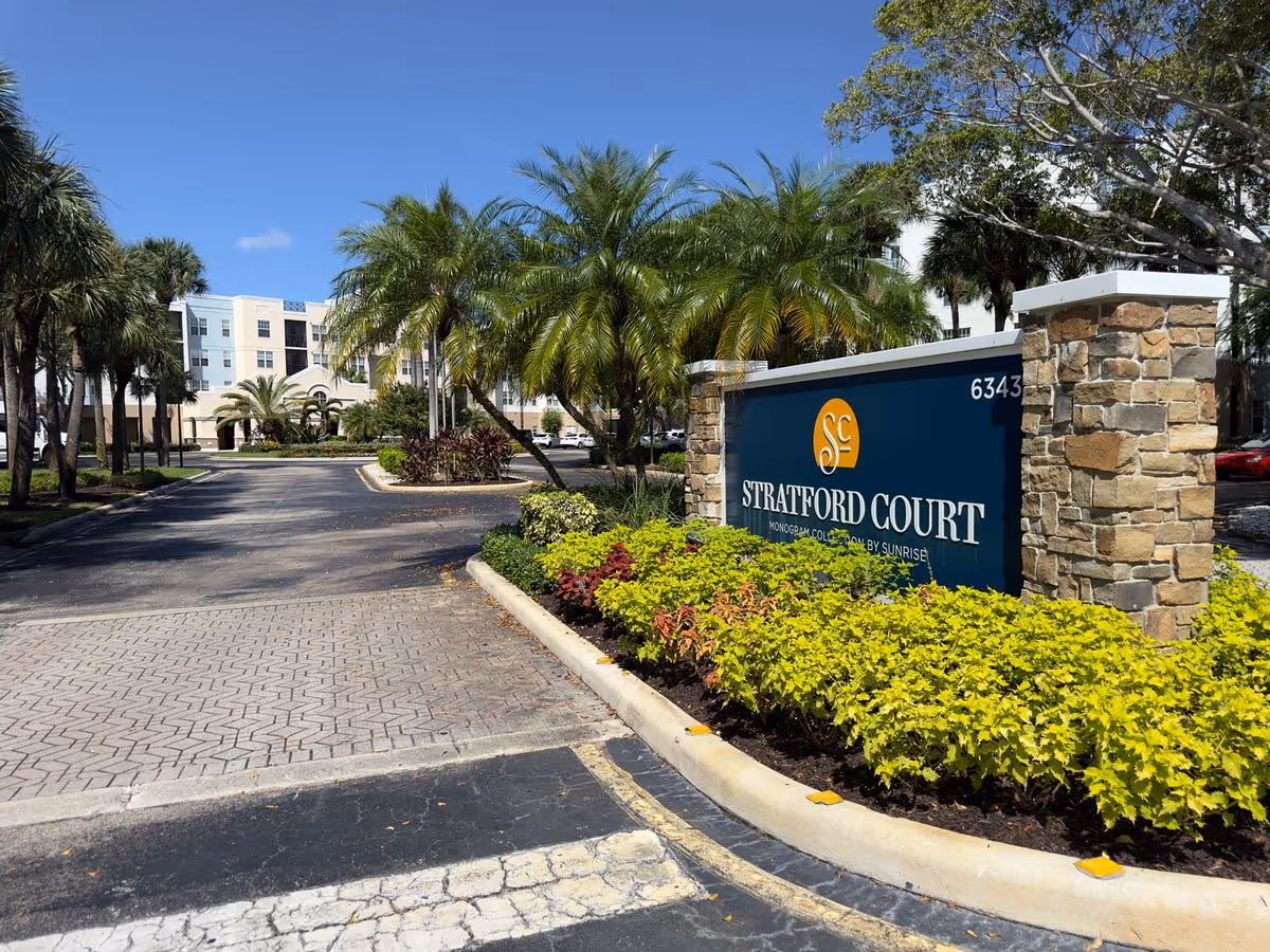 Landscaped entrance with a Stratford Court sign, palm trees, and a multi-story building beyond.