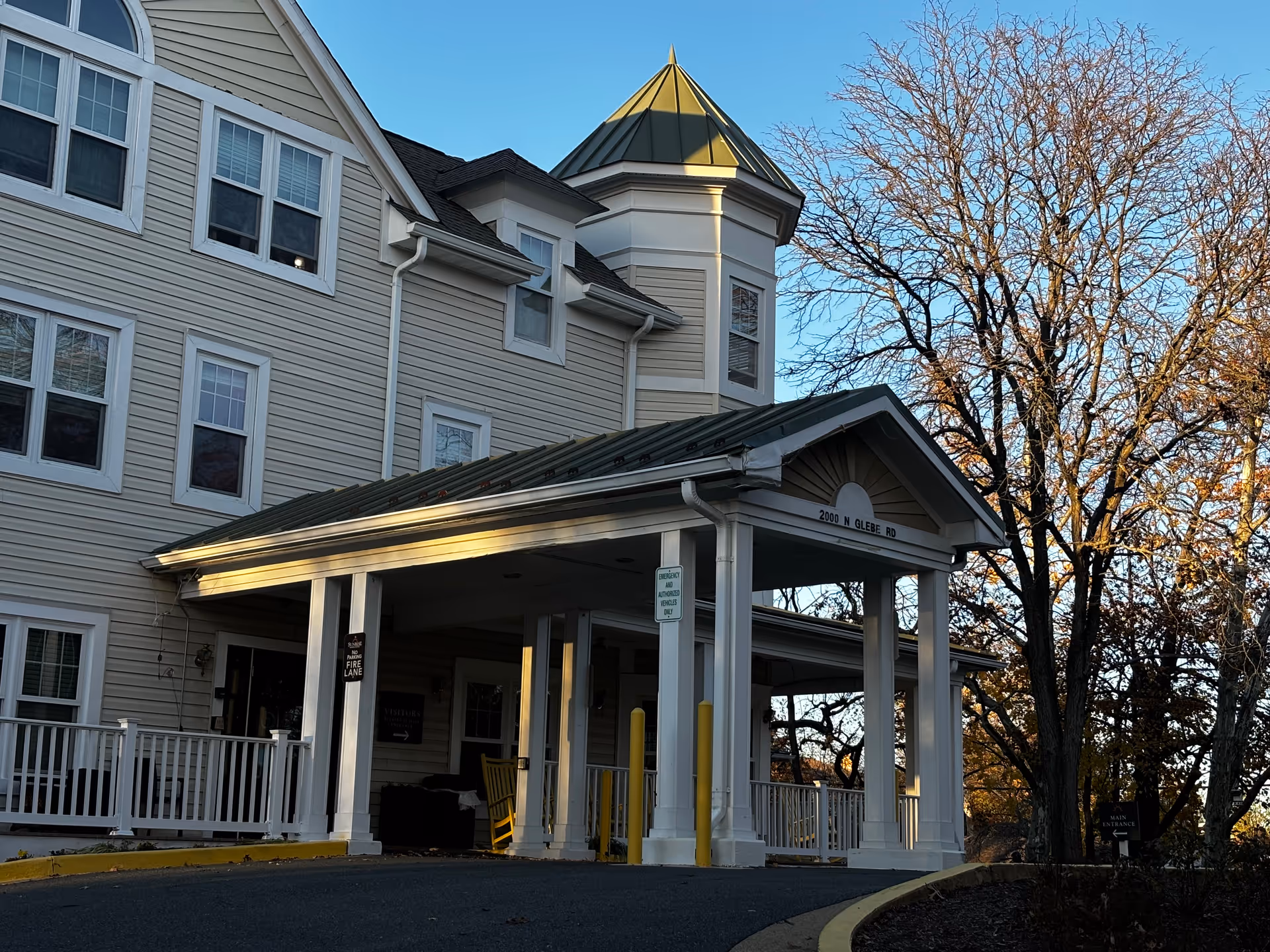 Exterior front entrance of a multi-story senior living building with a covered porte-cochere, white columns, and a small turret.