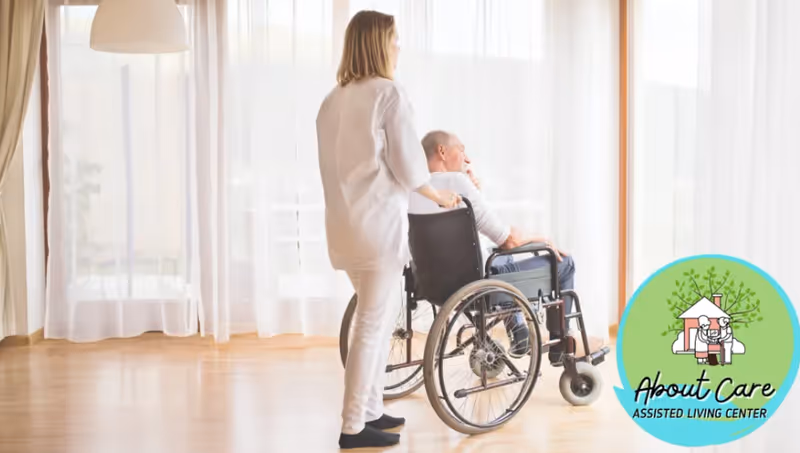 A caregiver standing behind and pushing a wheelchair with an elderly man seated in it, in a bright room with large windows covered by sheer white curtains.