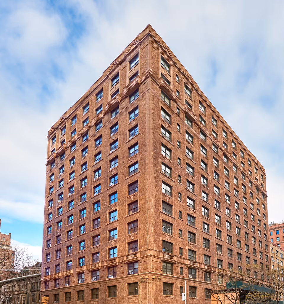 Corner view of a tall multi-story red brick building against a partly cloudy sky.