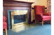 Brass-screened fireplace flanked by two red upholstered armchairs on blue carpet in a lounge area.