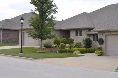 Single-story senior living facility exterior with manicured lawn, shrubs, and a driveway.
