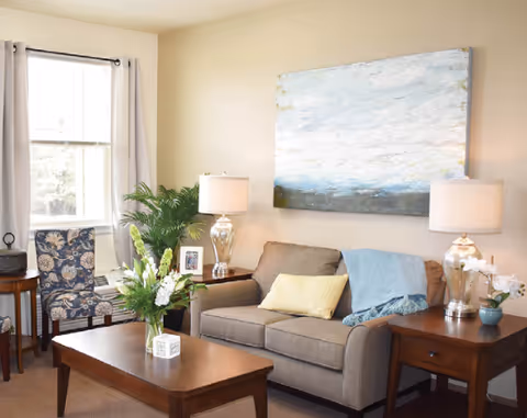 Cozy living room with a sofa, coffee table, side tables with lamps, a floral accent chair, and a large piece of wall art.