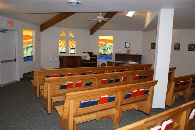 Interior chapel with wooden pews, stained glass windows, and an altar at the front.