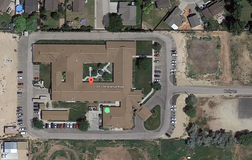 Aerial view of a large U-shaped senior living facility with a central courtyard, surrounding parking lots, and adjacent roads.