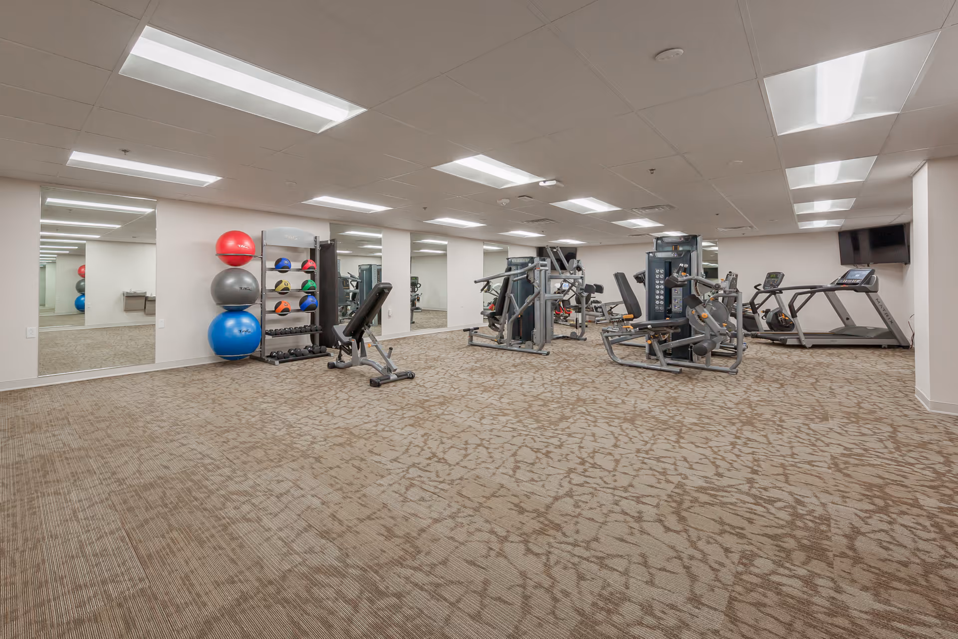 Spacious fitness room with weight machines, treadmills, benches, and exercise balls against mirrored walls.