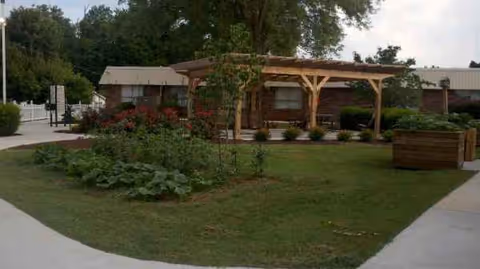A landscaped outdoor area with a wooden pergola near a low brick building.