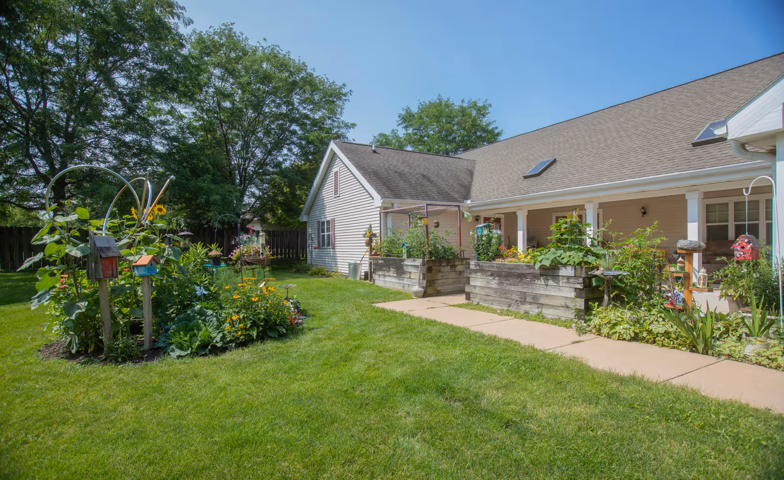 Front exterior of a single-story assisted living building with a porch, raised garden beds, and a grassy courtyard.