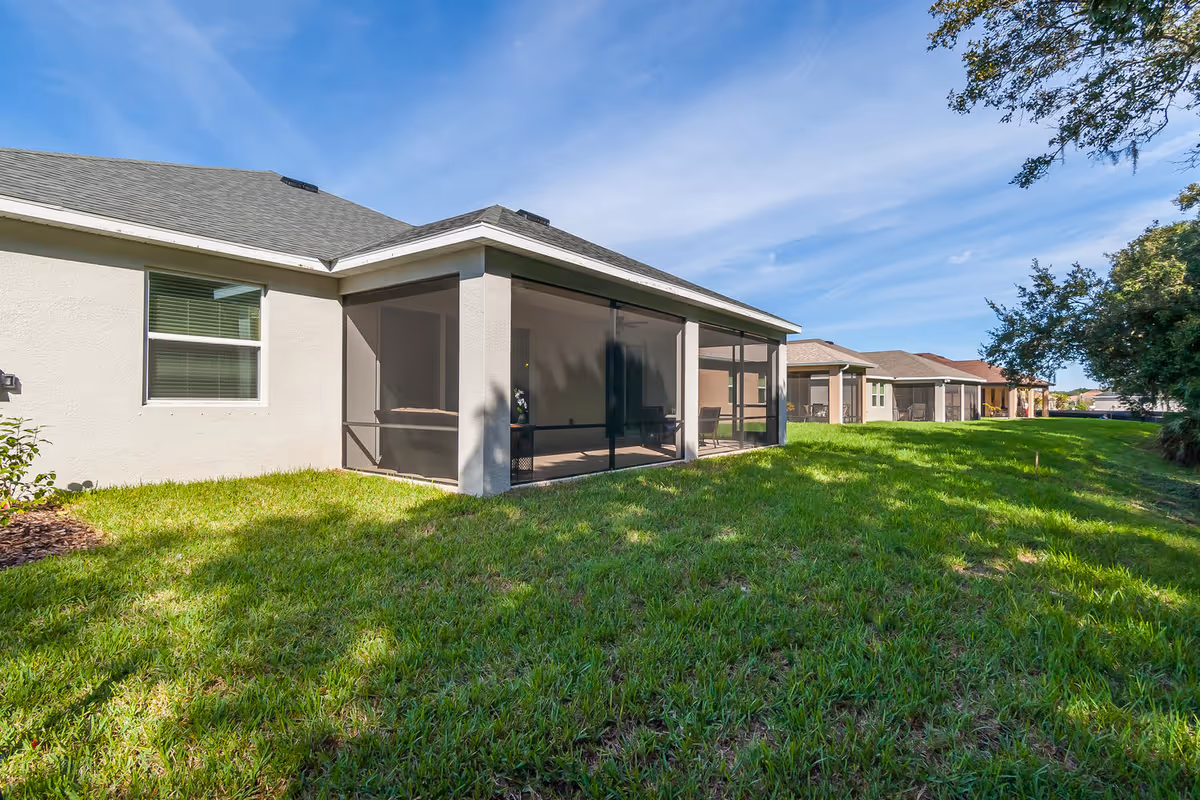 Single-story residential units with screened-in porches facing a green lawn under a blue sky.