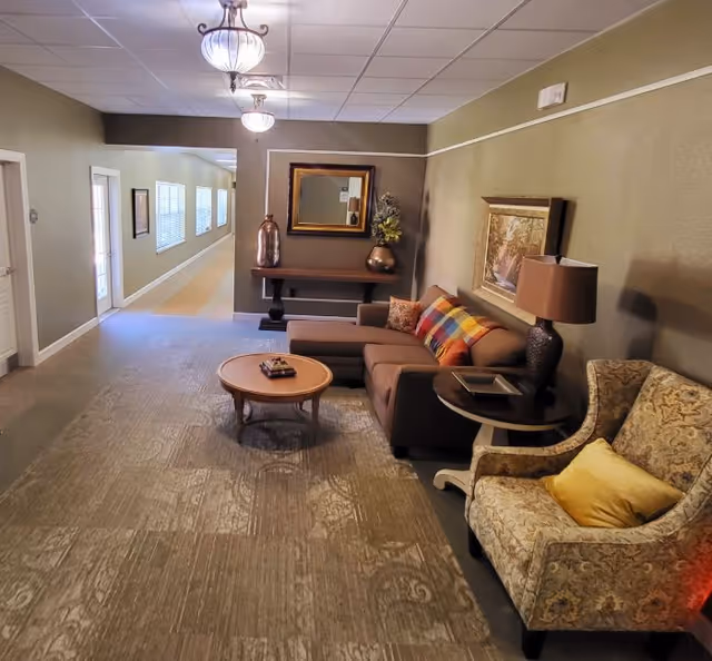 Furnished common lounge with a sectional sofa, armchair, coffee table, lamps and a hallway leading to doors.