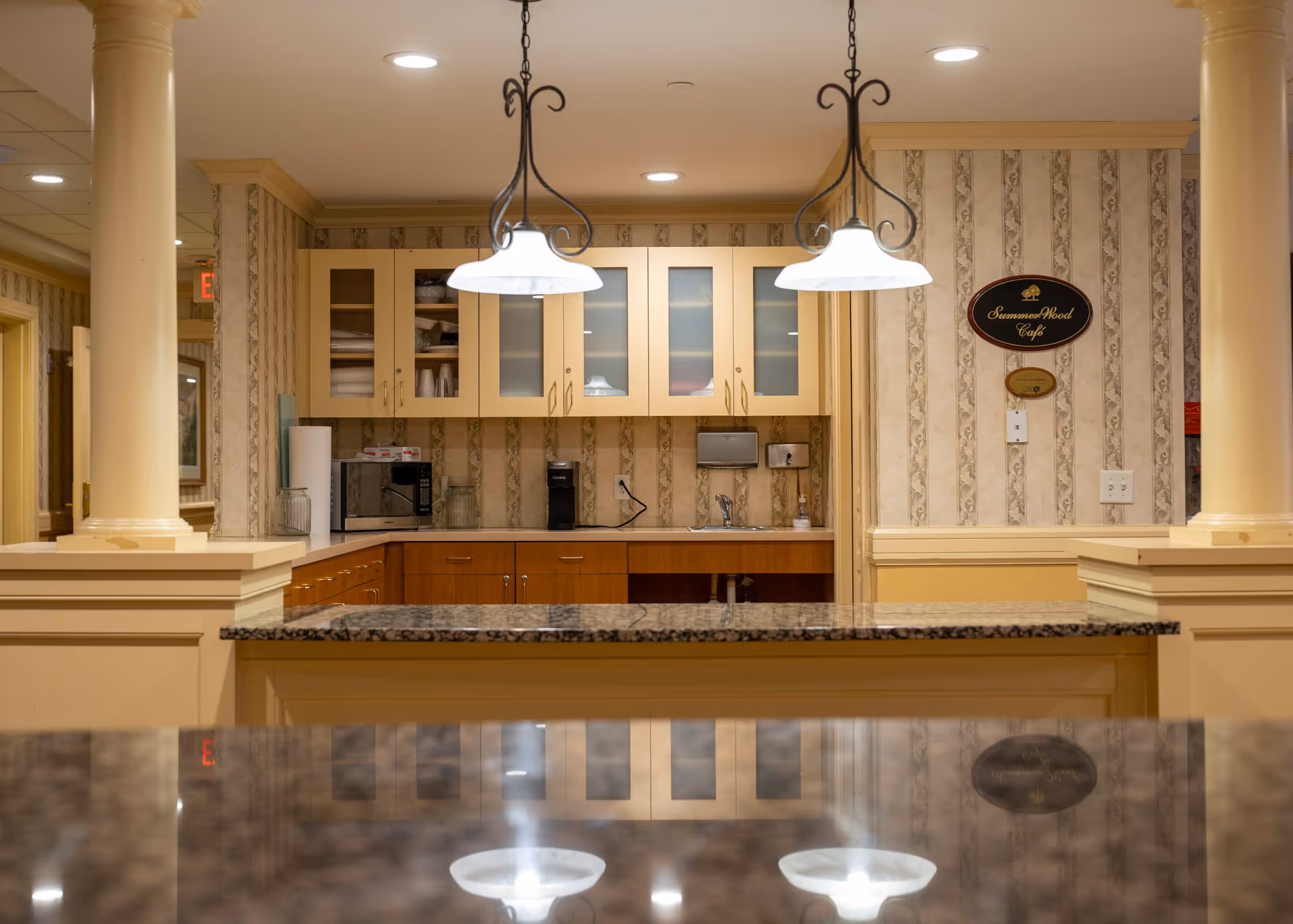Interior view of a senior living facility café counter with pendant lights, granite-topped bar, cabinets, and a 'SummerWood Café' sign.