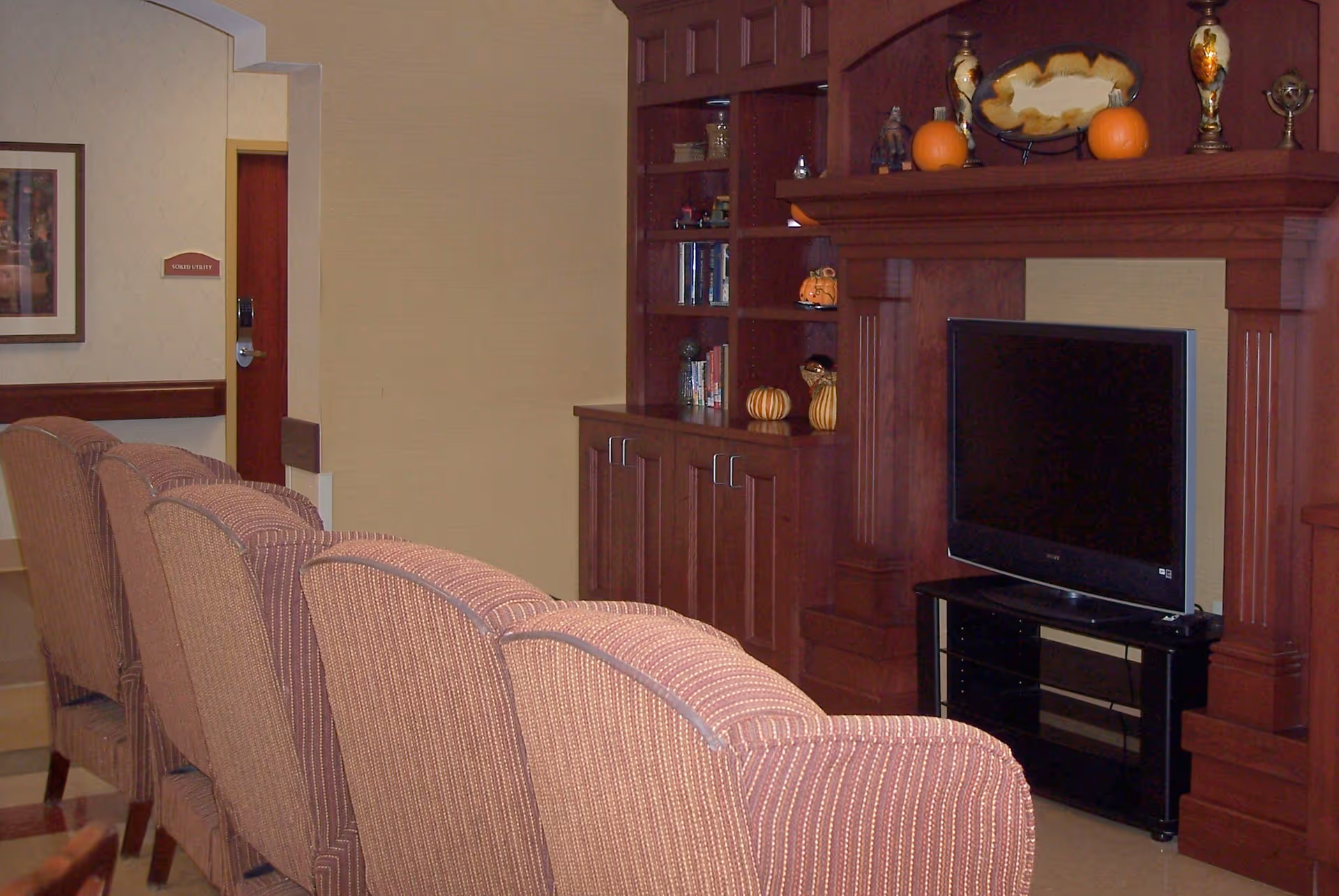Row of upholstered chairs facing a flat-screen TV and built-in wooden cabinetry in a common living area.