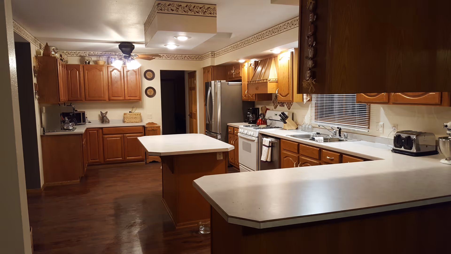 Spacious traditional kitchen with wooden cabinets, a central island and a long white countertop/breakfast bar with appliances.
