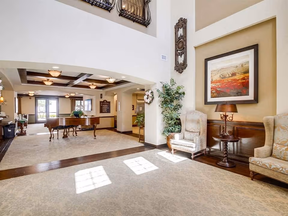 Sunlit senior living facility lobby with a grand piano, armchairs, and framed artwork.