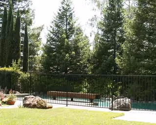 Outdoor view of a fenced pool area with a bench and lush trees.