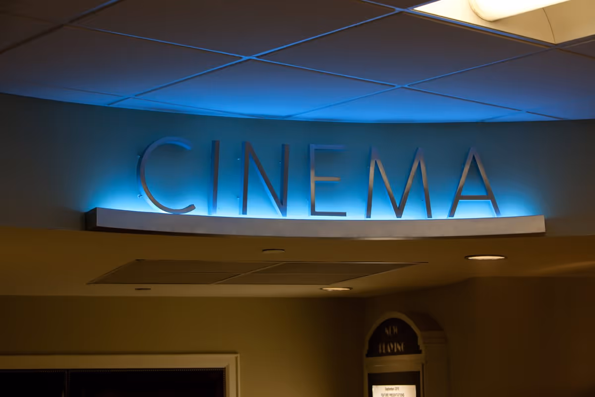 Illuminated sign with the word 'CINEMA' in large letters mounted on a wall with a blue backlight in an indoor setting.