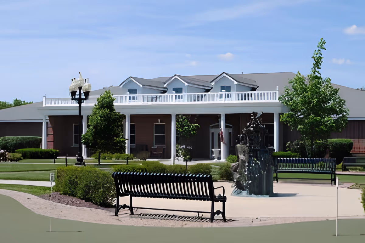 Front exterior of the Cottages of New Lenox showing the building entrance, benches, fountain, and landscaped lawn.