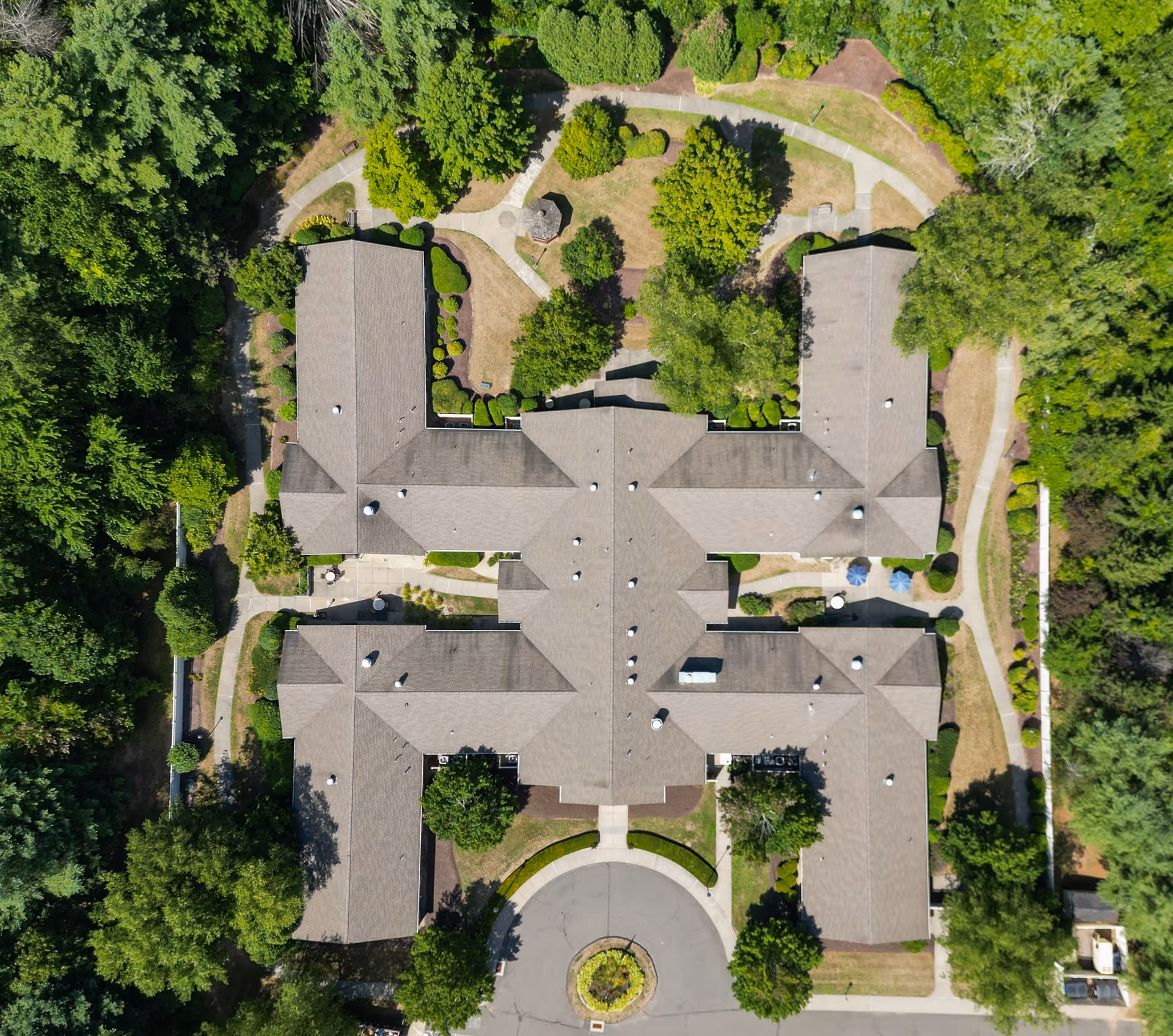 Aerial view of Arden Courts - ProMedica Memory Care Community (Avon) showing the building's roof surrounded by landscaped gardens, trees, and walking paths.